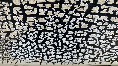 Foto Close-up of cracked paint surface with irregular cream fragments over dark base,