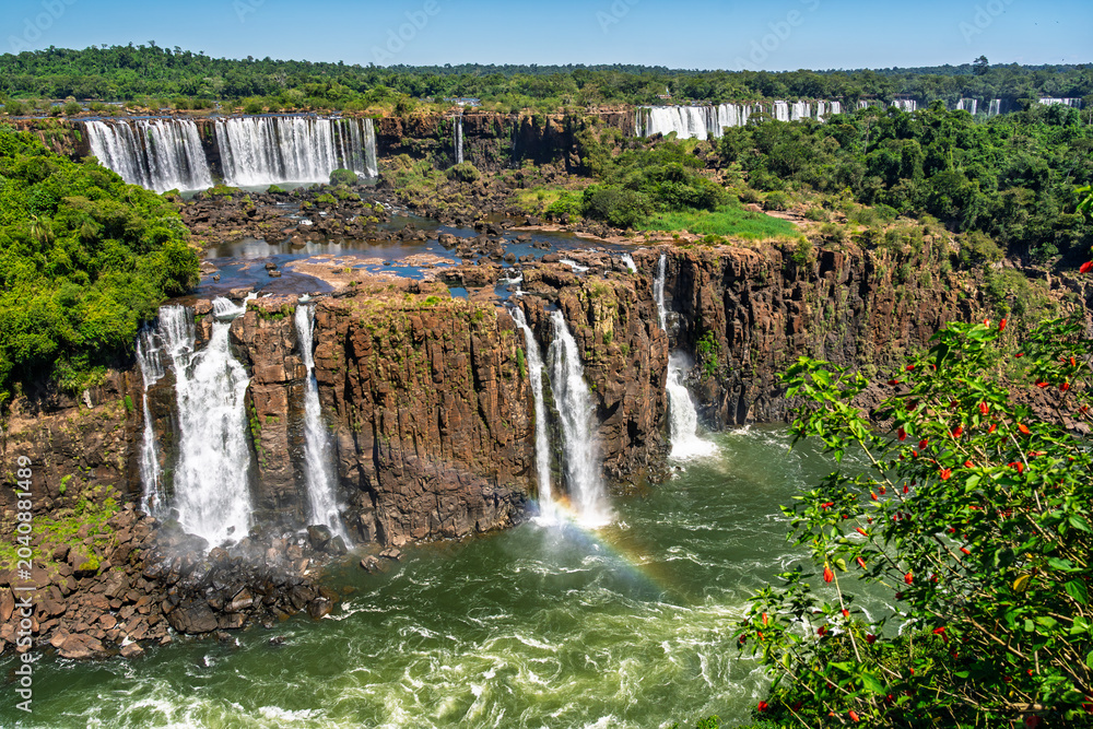 Obraz premium Panoramic view of Iguazu Falls in Iguazu National Park with rainbow and lush tropical rainforest