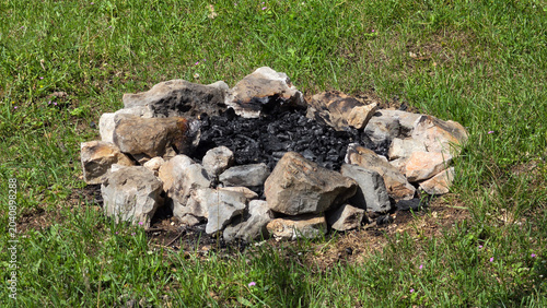 Photos Extinguished stone campfire ring filled with black charcoal chunks on a green gr
