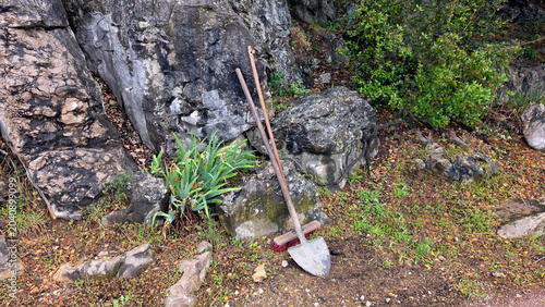 Photos Vintage garden shovel and push broom leaning against a large grey rock formation