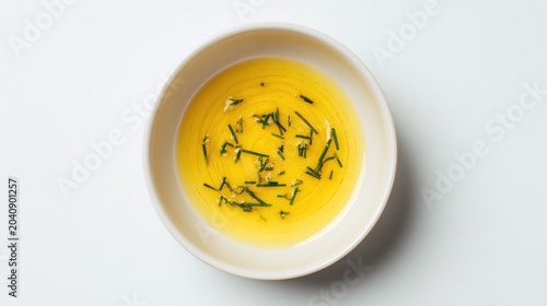 A white bowl contains golden liquid with finely chopped green herbs