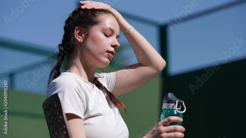 Young woman feeling exhausted from the heat during a tennis match break. The female athlete pours water from a bottle over her head to cool down