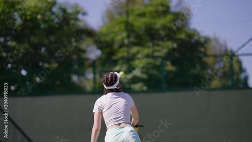 Professional female athlete performing a serve on an outdoor hard court. A focused woman practicing her tennis skills during a match