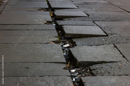 Broken stone pavement cracks in perspective. Concrete slabs shift causing damage. Urban footpath needs repair. Ground texture shows decay. City street maintenance issue.