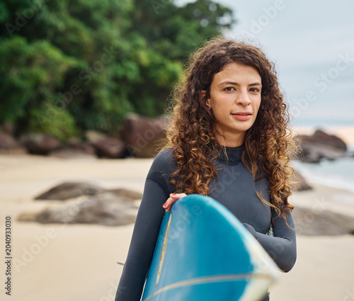 Photography Portrait of a young woman surfing at the beach, holding surfboard, ocean waves,