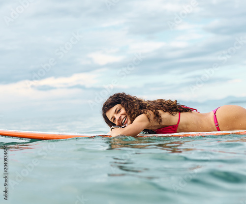 Photography Portrait of a young woman surfing at the beach, holding surfboard, ocean waves,