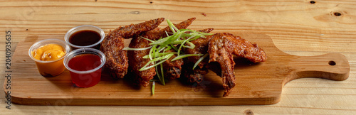 Φωτογραφία close up photo of chicken wings with 3 kinds of dipping sauce which is honey mustard, sweet and sour and buffalo sauce on a wooden plate