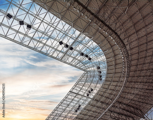 Modern steel roof structure of a stadium against a beautiful sunset sky.
