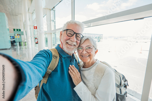 Фотография Senior couple widely smiling and taking a cheerful selfie in a bright airport te