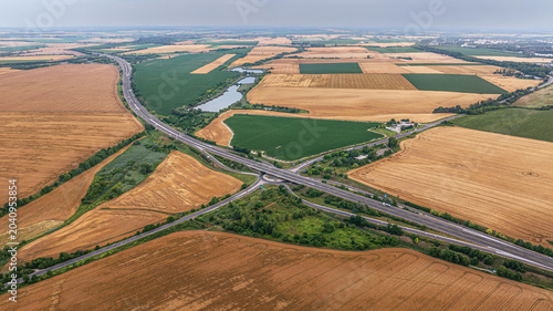 Fotografía Highway Interchange in Agricultural Landscape – Wide drone aerial view of highway junction surrounded by farmland and rural terrain