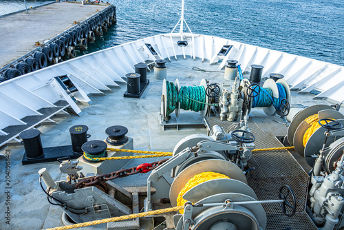 View from the deck of a ship showing winches and ropes with water in the background during the day