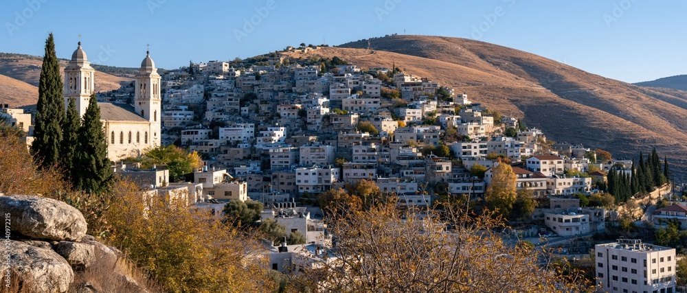 Obraz premium This image showcases a picturesque hillside village with stunning architecture set against a backdrop of rolling hills and clear blue skies, representing tranquility and beauty.