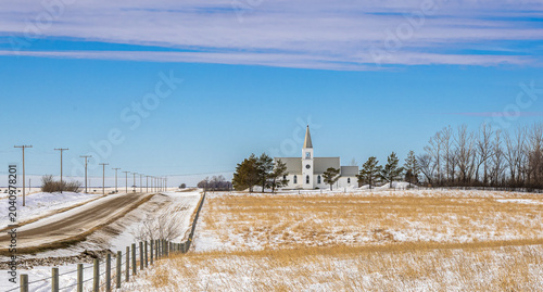 Photos A historic rural church set against a vast winter prairie landscape, featuring distinctive white steeple, a typical Saskatchewan landmark representing the settlement history of Canadian prairies