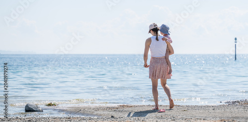 Fotografía Mother carrying child walking to sunny beach lake constance