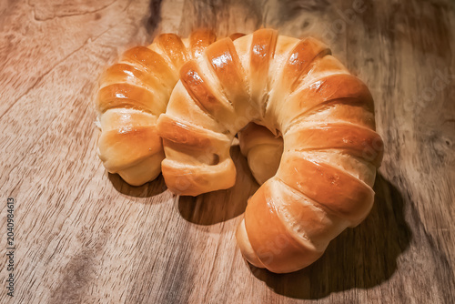 Fresh Golden Crescent Bread Rolls on Rustic Wooden Table.  Freshly baked golden crescent bread rolls with a glossy crust arranged on a rustic wooden tabletop. Warm natural tones, artisan bakery style.