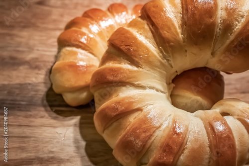 Fresh Golden Crescent Bread Rolls on Rustic Wooden Table.  Freshly baked golden crescent bread rolls with a glossy crust arranged on a rustic wooden tabletop. Warm natural tones, artisan bakery style.