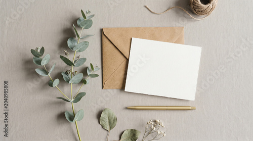 Minimalist Blank White Card, Craft Envelope, and Eucalyptus Sprig on Rustic Linen Background Flat Lay