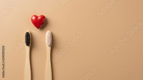 Two Natural Bamboo Toothbrushes With a Red Heart on Beige Background for Eco-Friendly Oral Care.