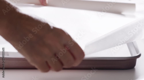 Hand lines a baking tray with parchment paper during food preparation in a kitchen. High quality 4k footage