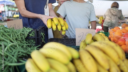 Bilde på lerret Family shopping for fresh, organic bananas and green beans at a vibrant local fa