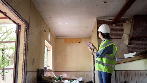 Foto Female surveyor in hard hat and safety vest inspects and documents structural da