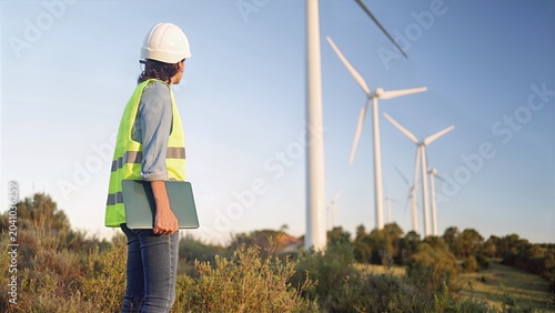 Quadro su tela Female engineer in safety vest and hard hat holding a laptop, standing at a wind