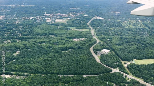 Airplane wing overlooks a winding road crossing dense forest and rural terrain from high altitude during flight. High quality 4k footage