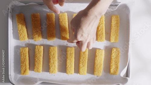 Hands arrange breaded fish sticks on a parchment lined baking tray before oven cooking. High quality 4k footage