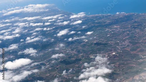 Scattered clouds drift above a vast countryside landscape viewed from high altitude during flight. High quality 4k footage