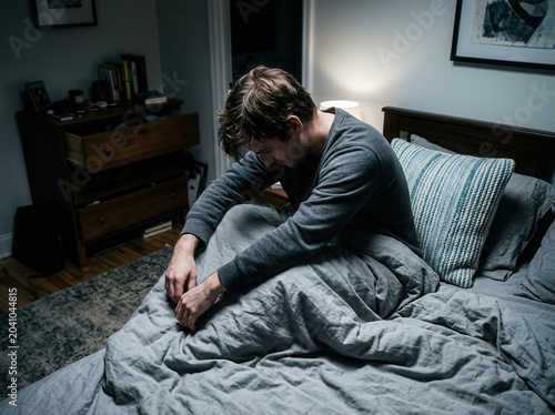 A Person In Distress Sitting On A Bed Reflecting Deeply In a Somber And Dark Bedroom