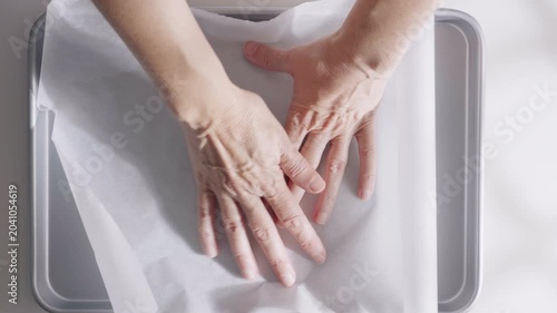 Hands place and adjust parchment paper inside a baking tray during kitchen food preparation. High quality 4k footage