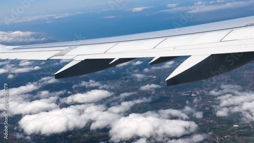 Airplane wing extends above scattered clouds and distant landscape during a high altitude flight. High quality 4k footage