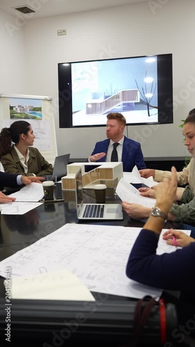 Business team of architects and engineers meeting in the office conference room to discuss a new building project with blueprints and model