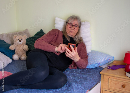 Senior woman using smartphone with serious expression lying on bed at home