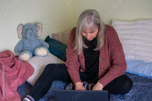 Senior woman using laptop lying on bed focused on screen at home