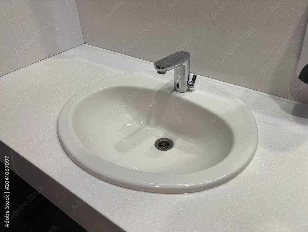Fototapeta premium Modern white vanity unit with a ceramic sink and faucet in a public restroom or office bathroom