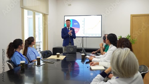 Professional business manager presenting a slideshow with charts and graphs to a team of doctors and nurses in a hospital board meeting