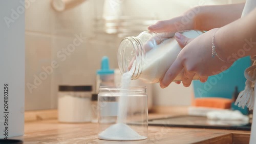 Home baker carefully adds sugar to jar. Precise motion captures sugar pouring into glass jar during morning. Warm morning light highlights baker skillfully measuring and pouring sugar into jar