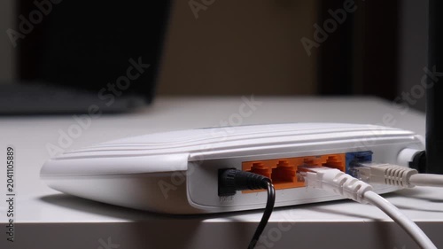 Person's hands connecting a white ethernet cable into the lan port of a white wireless router, setting up internet connection and network connectivity on a modern desktop