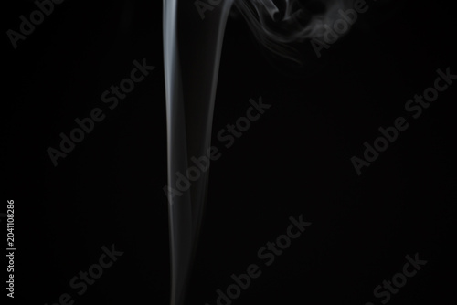 A white curved texture, magical smoke from an incense stick rising from the surface against a dark black background with copy space. Mystical pattern, concept of meditation and relaxation. Magical fog