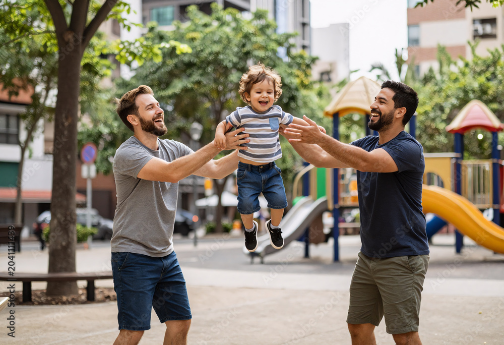Obraz premium Happy gay parents playing with toddler in park