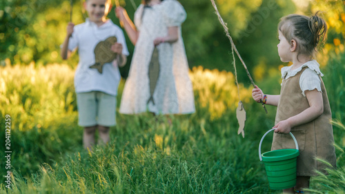 Fotografía Children playing pretend fishing in a sunny meadow with green grass and trees