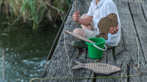 Canvastavla Child playing pretend fishing with cardboard fish and bucket on a wooden pier