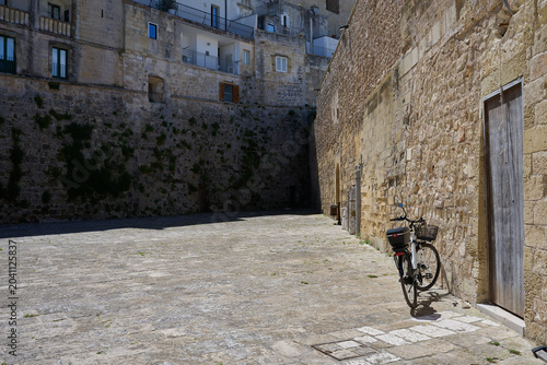 Single push bike leaning against a yellow brick wall next to an old doorway in historical part of Otranto Puglia southern italy