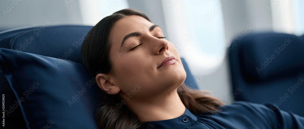 Fototapeta premium A serene image of a woman resting comfortably on an airplane seat, embodying relaxation and peace amidst travel, evoking feelings of comfort and tranquility.