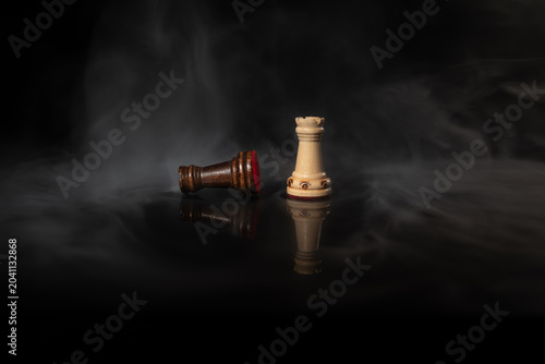 Fotografía Standing chess rook facing a fallen rook on a dark smoky background, symbolizing rivalry, victory, defeat, strategy, conflict, leadership, pressure and high‑stakes decision‑making