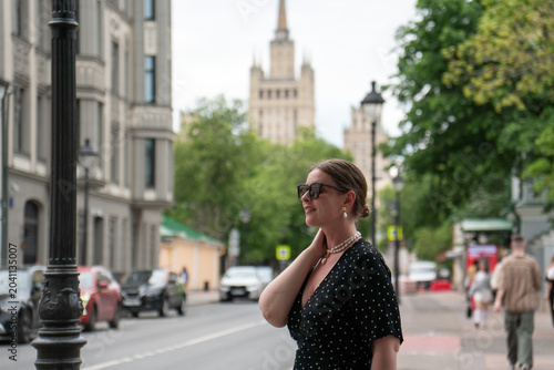 Bild auf Leinwand Woman in black polka dot dress stands on Malaya Nikitskaya Street in Moscow, with Kudrinskaya Square skyscraper, historic urban architecture framing scene