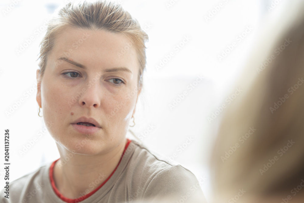 Fototapeta premium Female individual with light brown hair wearing a beige shirt, gazing thoughtfully while seated indoors with soft natural light illuminating the scene