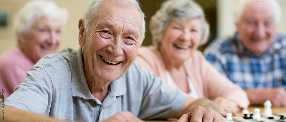 Fototapeta premium This heartwarming image of elderly friends smiling and playing chess captures the joy of companionship and intellectual engagement in their golden years.