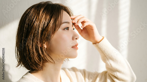 A young woman with short brown hair touching her forehead in a white sweater